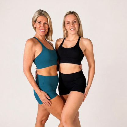 Two women wearing 'Emma' Pole Shorts and matching sports bras, showcasing comfort and style for pole fitness.