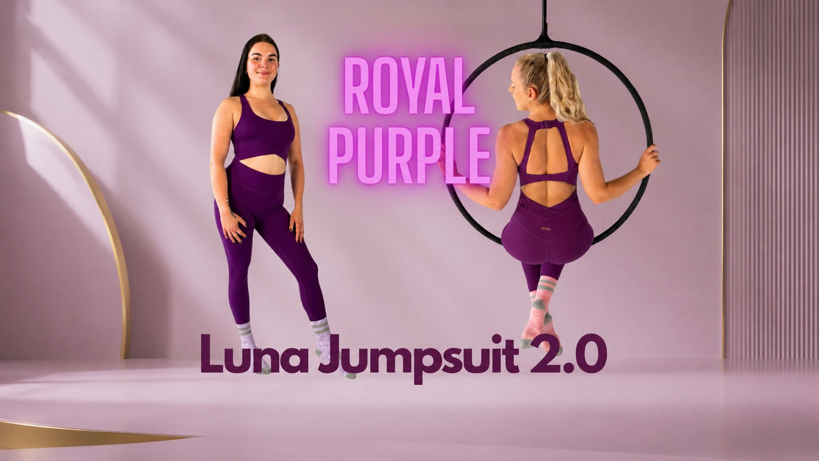 Two women modeling a purple athletic jumpsuit in a stylized studio setting. One stands facing forward on the left, and the other is suspended in a black aerial hoop on the right.
