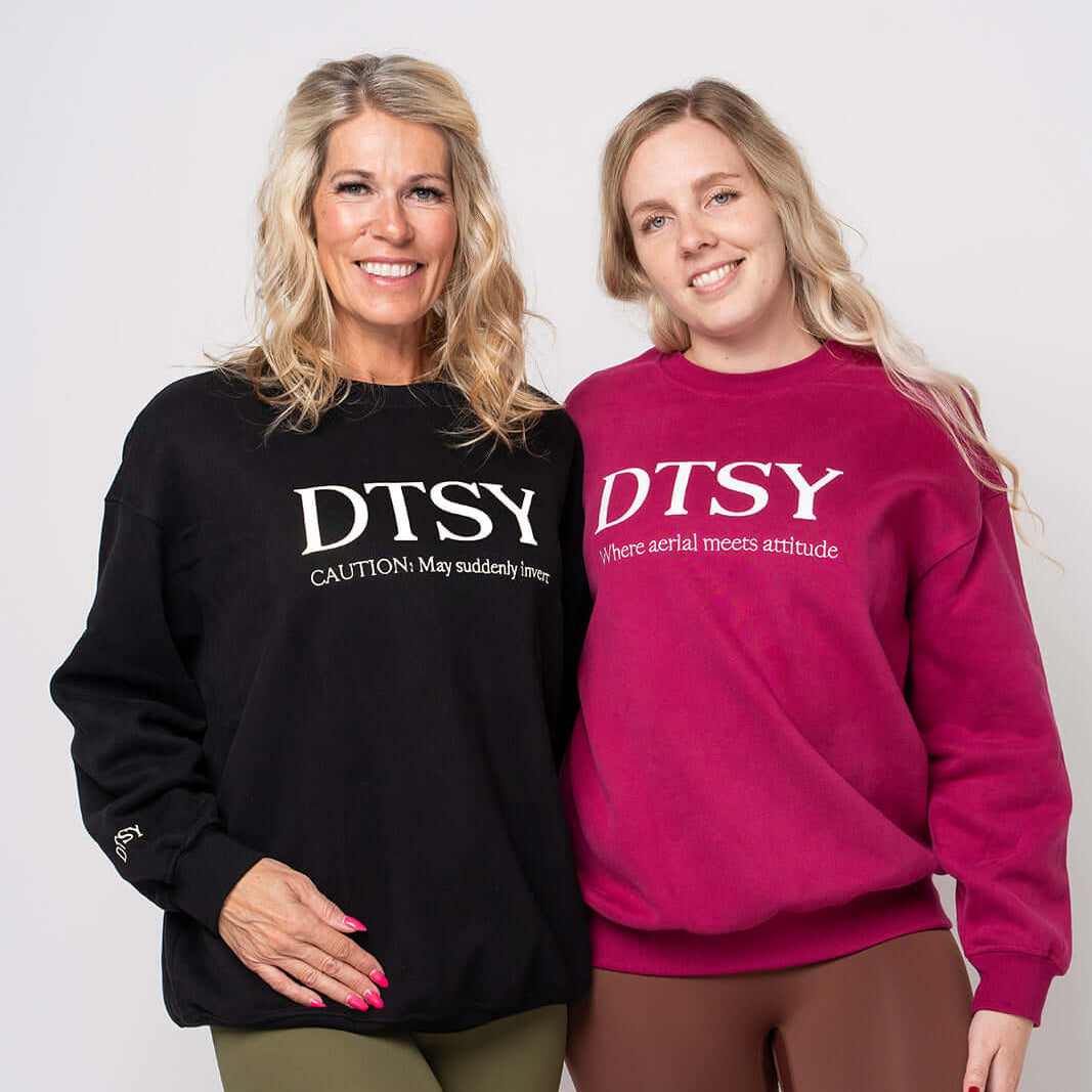 Two women modeling the DTSY Aerialist Jumper, showcasing styles in black and fuchsia with playful slogans.