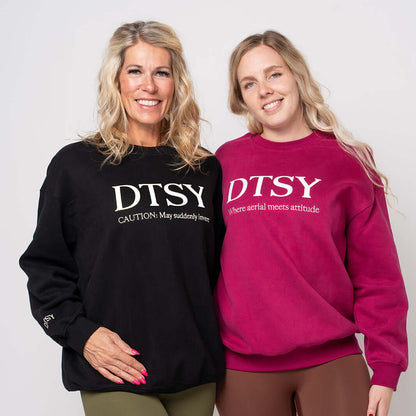 Two women modeling the DTSY Aerialist Jumper, showcasing styles in black and fuchsia with playful slogans.