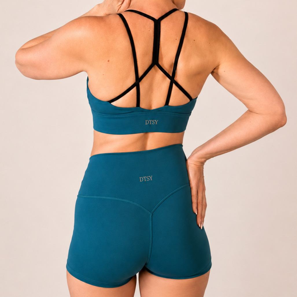 Woman wearing a emerald green sports bra with black straps, pole shorts set on a beige background